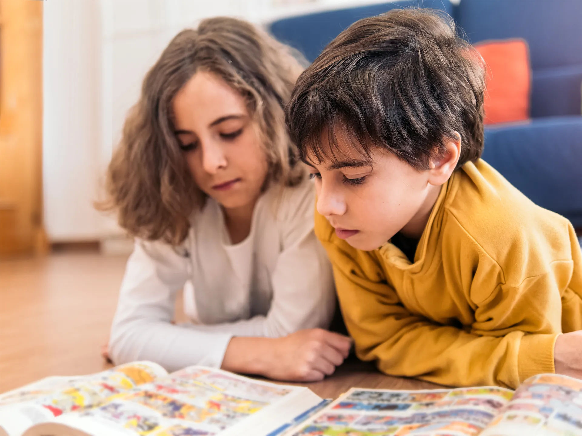 Ein Mädchen und ein Junge liegen auf dem Boden und lesen Comic-Buecher