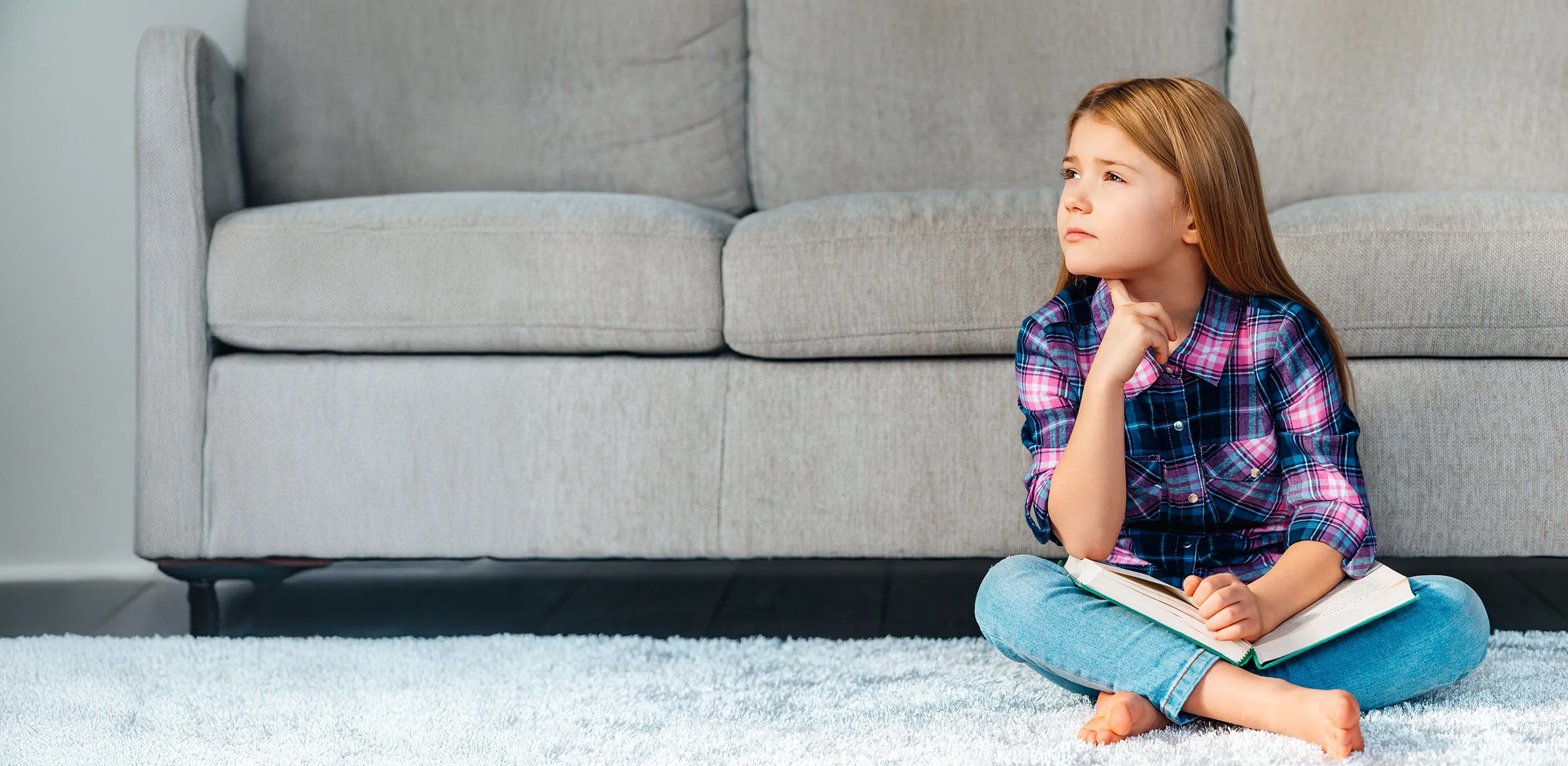 Kind sitzt auf dem Teppich vor einer Couch und denkt nach
