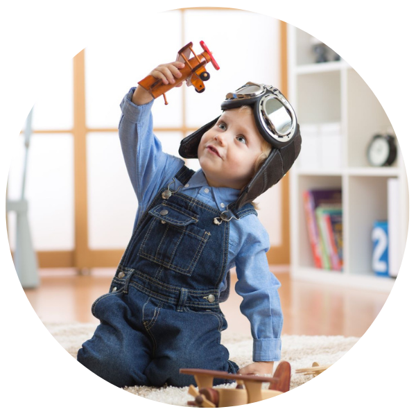Kind mit Latzhose und Fliegerbrille, das mit Flugzeugen spielt
