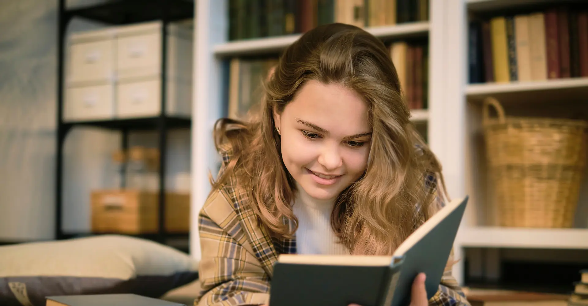 Junges Mädchen liest ein Buch, im Hintergrund ein Bücherregal