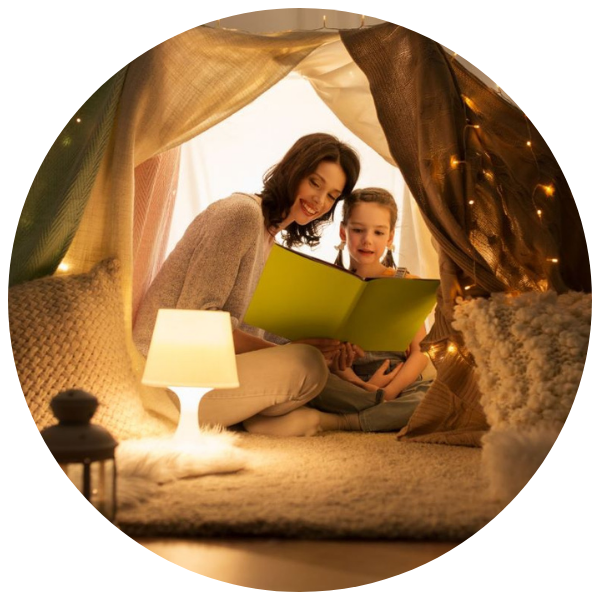 Bilderbuecher für Kleinkinder; Vorlesen gemütliche Kuschelhöhle mit Lichterketten und Kissen, in der eine Mutter ihrem jungen Mädchen etwas aus einem Buch vorliest; Linkziel: Tipps fuer Eltern