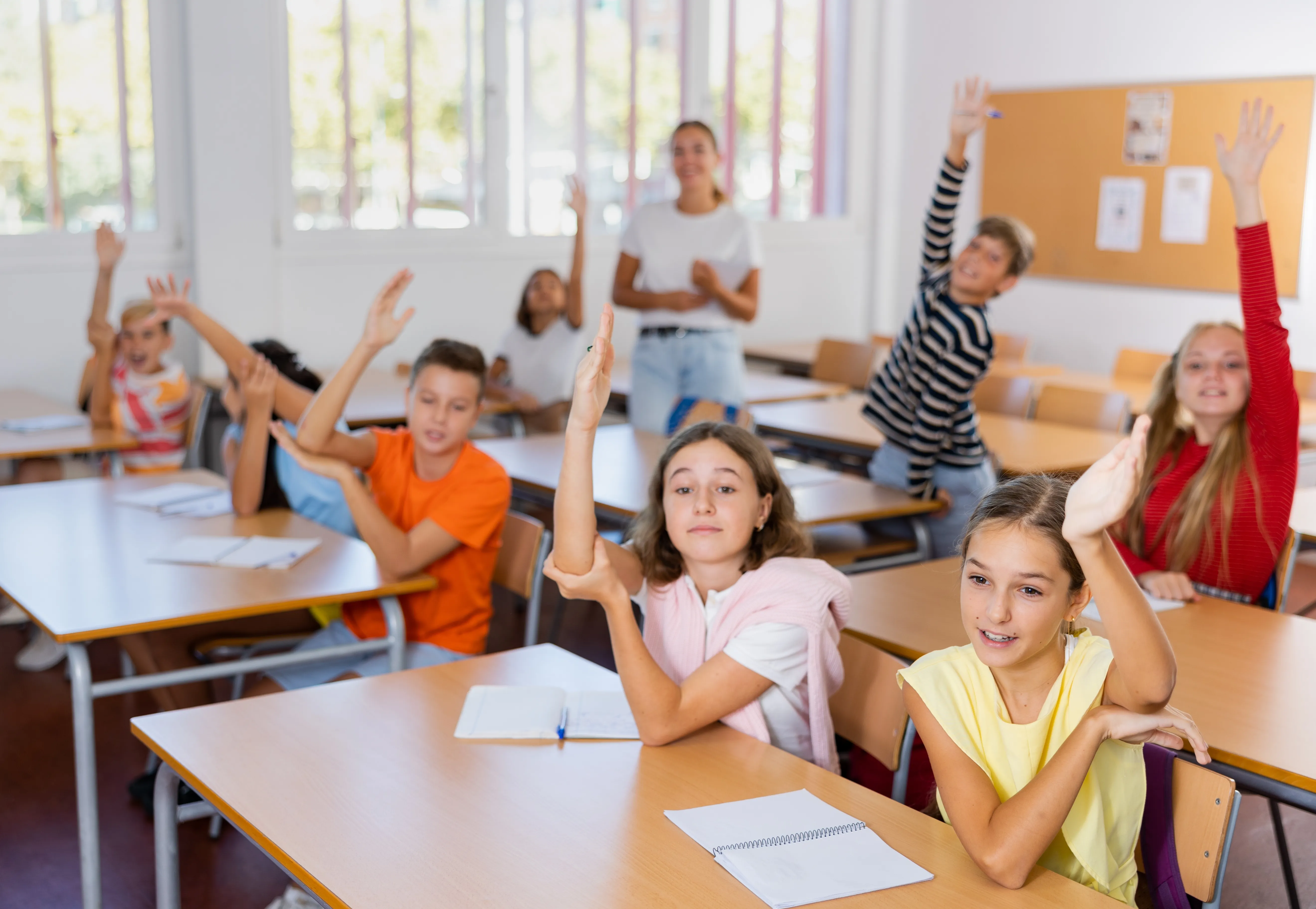 Bild einer Schulklasse in einem Klassenzimmer; Kinder heben die Hand